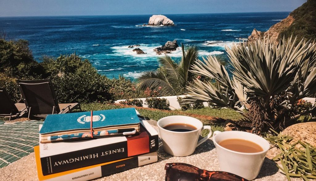 A cup of coffee, books, and sunglasses on a balcony overlooking nature, representing a quiet moment of celebration.