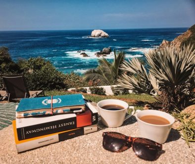 A cup of coffee, books, and sunglasses on a balcony overlooking nature, representing a quiet moment of celebration.