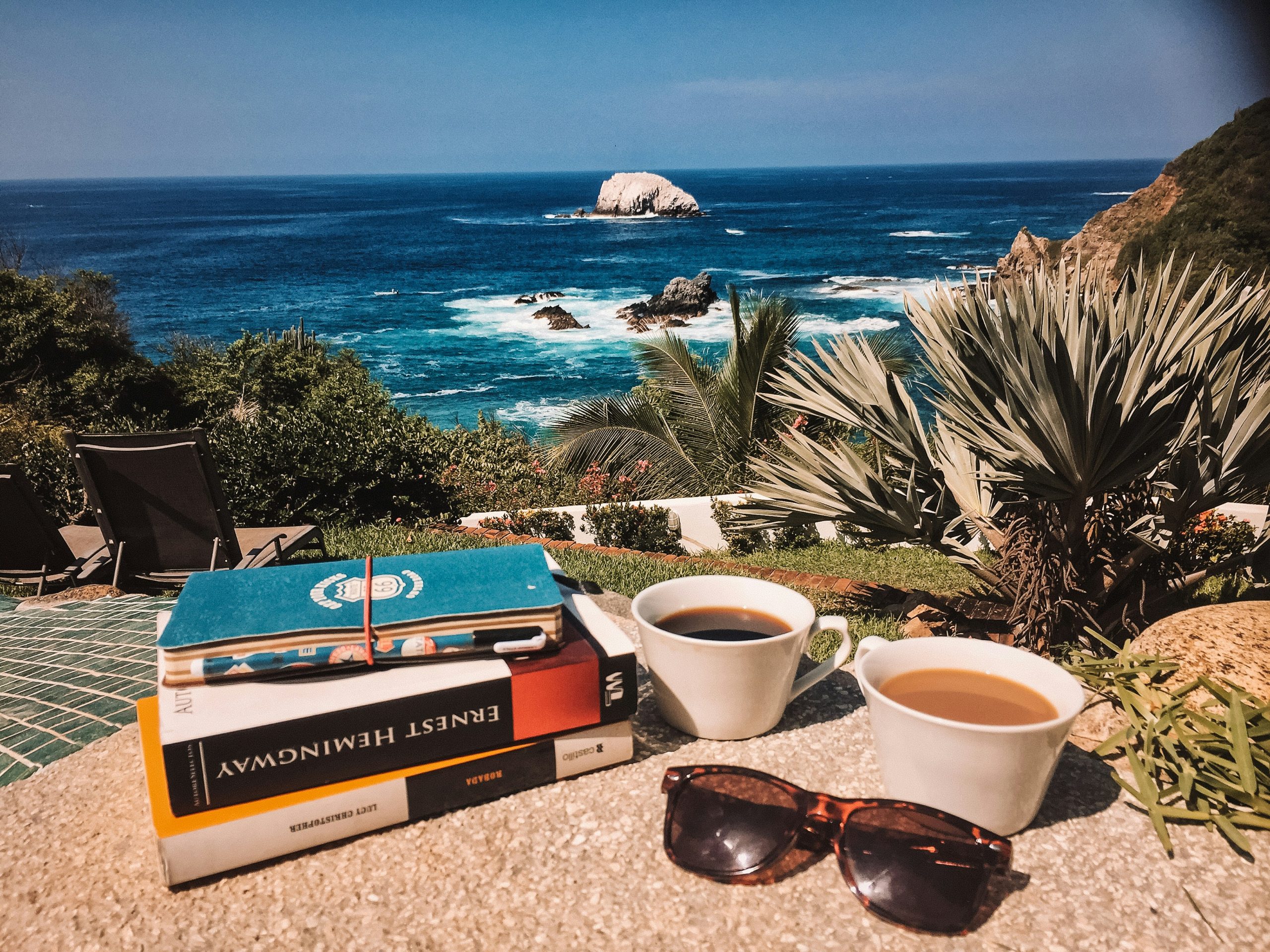 A cup of coffee, books, and sunglasses on a balcony overlooking nature, representing a quiet moment of celebration.